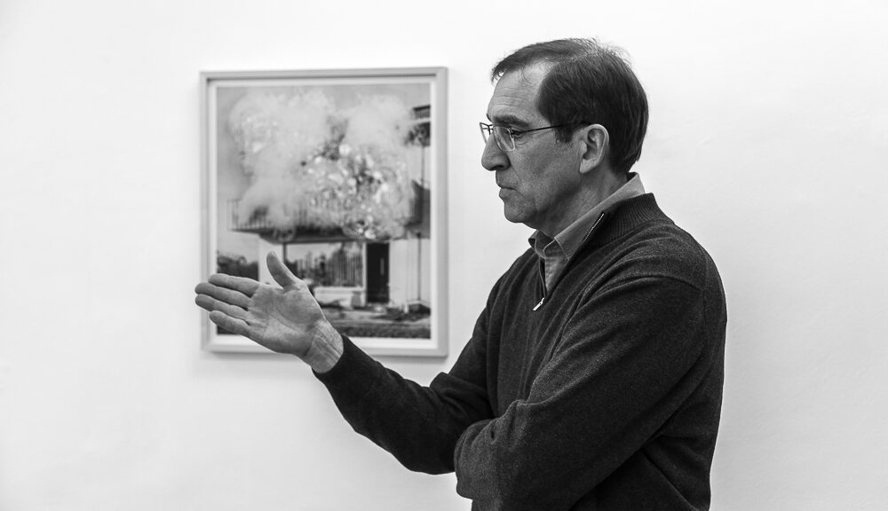 Künstler Christoph Dahlhausen mit ausgestreckter Hand, Hintergrund ein hängendes Werk