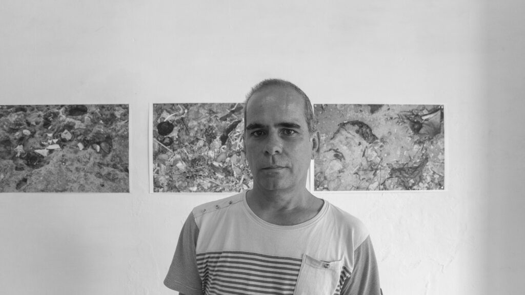 black and white portrait of Alfredo Ramoz Fernandez, background prints on the wall