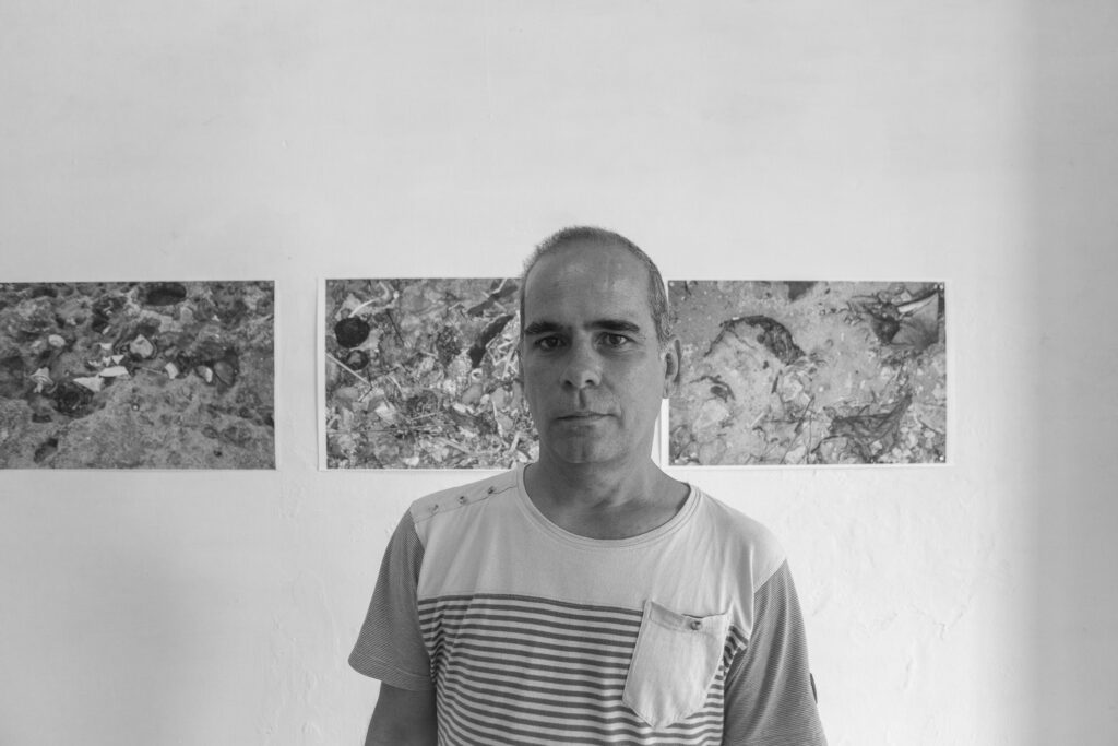 black and white portrait of Alfredo Ramoz Fernandez, background prints on the wall