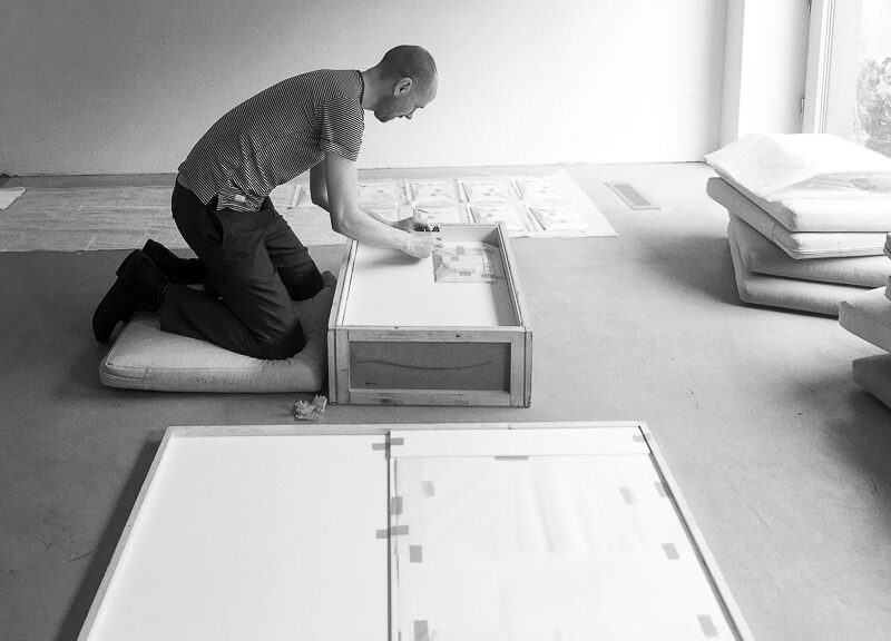 Künstler Eric Cruikshank sitzt auf dem Boden und bereitet seine Werke für die Ausstellung vor