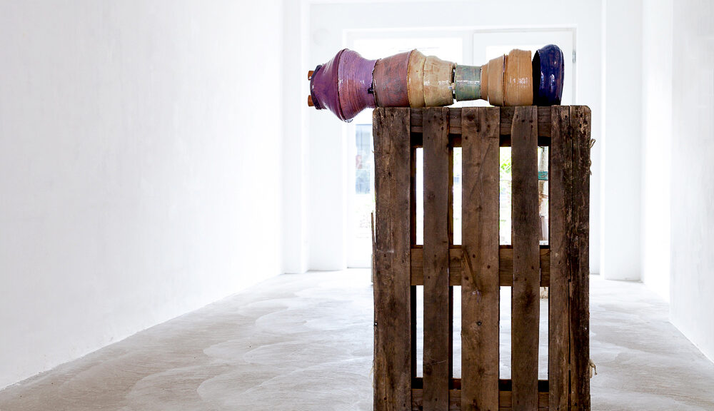 Ein Objekt bestehend aus einer Holzpalette und einem mehrfarbigen Konstrukt aus Keramik.