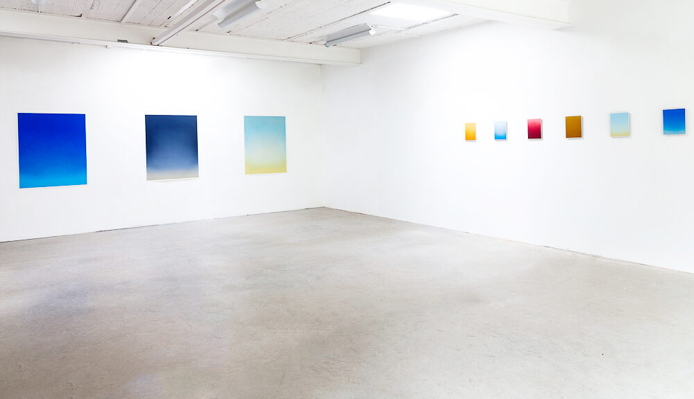 Ausstellungansicht, man kann zwei weiße Wände sehen, auf der linken sind 3 blaue Werke zu sehen, auf der rechten Wand 6 kleinformatige Werke.