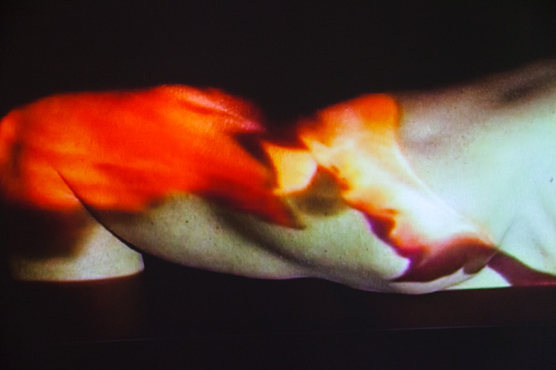 Detailaufnahme der Videoprojektion, Nahmaufnahme eines Oberarms, der orange angeleuchtet wird