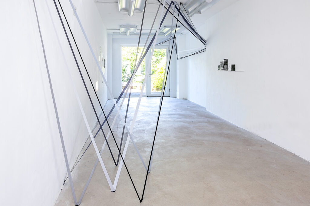 Ausstellungsansicht: (Vordergrund) Felicity Clear, Seídeán, ortsspezifische Installation Elastic and Paper Tape, Dimensions Variable, 2024 – (rechts) Kiera O`Toole, Felt Map, Altona, Hamburg, Germany. variable Dimensionen, mixt Media, 2024 | image: ©das_esszimmer